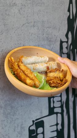 Assiette en bois contenant des nems, des crevettes et des chips, présentée dans le restaurant asiatique BOLKIRI.