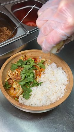 Un bol de riz blanc avec légumes et viande, agrémenté de coriandre, dans un restaurant asiatique.