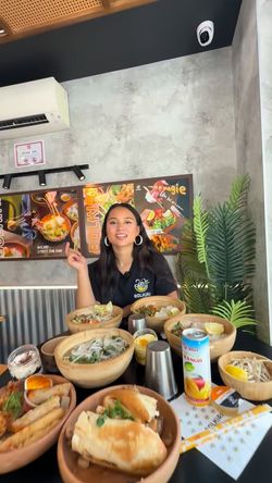 Restaurant asiatique BOLKIRI avec une femme au centre, entourée de plats vietnamiens variés sur une table.