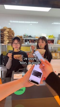 Deux employées dans un restaurant asiatique mangent derrière le comptoir, un paiement mobile est visible en premier plan.