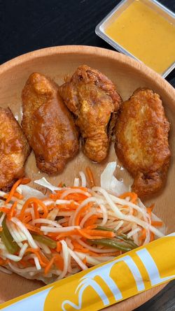 Ailes de poulet frites servies avec une salade de légumes marinés et une sauce jaune à côté.