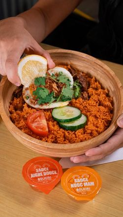 Plat asiatique avec riz rouge, légumes frais et viande assaisonnée, accompagné de sauces BOLKIRI sur une table en bois.