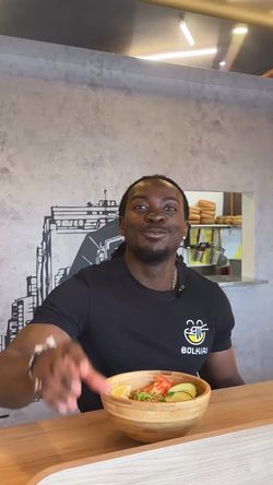 Client assis dans un restaurant asiatique, tenant un bol en bois avec des aliments variés devant lui.