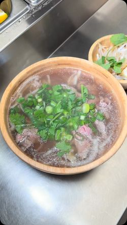 Soupe asiatique chaude dans un bol en bois garnie d'herbes fraîches et de morceaux de viande.