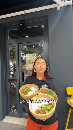Deux plats asiatiques servis dans des bols tenus par une femme devant le restaurant BOLKIRI Melun Street Food Viêt.