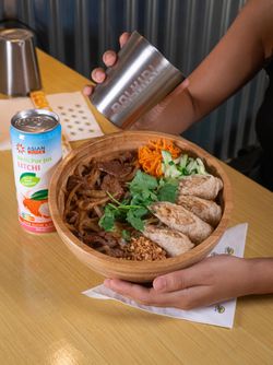 Plat asiatique dans un bol en bois avec légumes, viande et chips, accompagné d'une boisson au litchi sur une table.