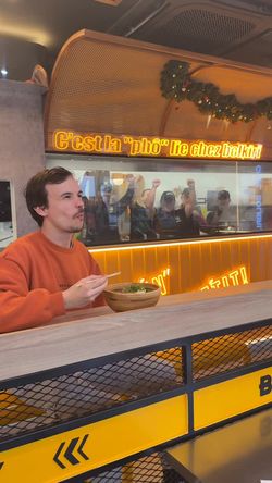 Intérieur du restaurant asiatique BOLKIRI avec une personne dégustant un bol de pho, décorations lumineuses en arrière-plan.