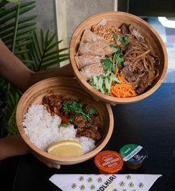 Deux bols en bois contenant riz, viande, légumes et nems, accompagnés de sauces et serviette du restaurant asiatique BOLKIRI