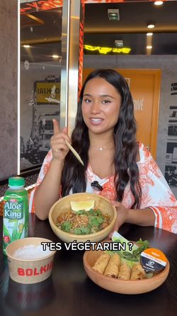 jeune femme tenant des baguettes, assise à une table dans un restaurant asiatique avec des plats vietnamiens et une boisson
