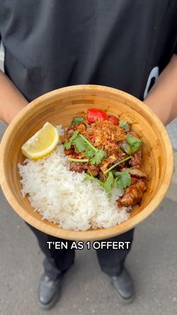 Plat asiatique servi dans un bol en bambou avec riz blanc, viande, légumes, citron et herbes fraîches.