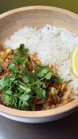 Plat asiatique avec du riz, des légumes sautés et de la coriandre, servi dans un bol en bois.