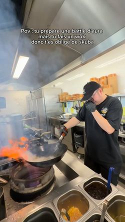 Cuisinier en tenue de travail préparant un wok avec une flamme dans une cuisine de restaurant asiatique.