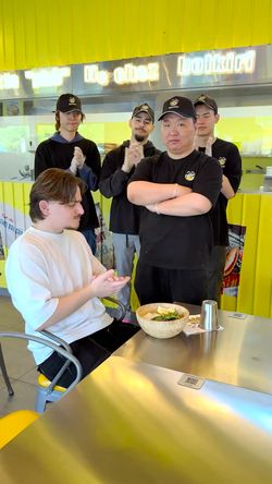 Un groupe de personnes sourit dans un restaurant, un client assis avec un plat de nourriture.