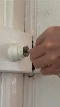 Une main tourne une clé dans une serrure fixée sur un mur intérieur blanc.