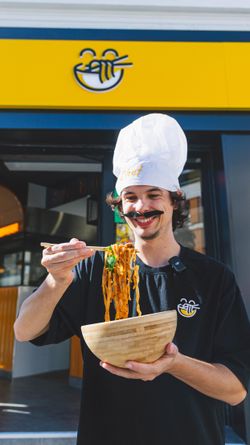 Un chef souriant présente un plat de nouilles dans un restaurant asiatique.