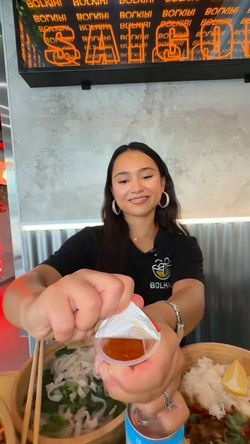 Serveuse dans un restaurant asiatique BOLKIRI versant une sauce sur un plat de street food vietnamienne.