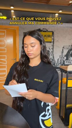 Femme dans un restaurant asiatique BOLKIRI, portant un t-shirt noir, lisant un papier dans un espace de restauration moderne.
