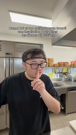 Cuisinier dans un restaurant asiatique en cuisine professionnelle avec équipement et étagères en arrière-plan.