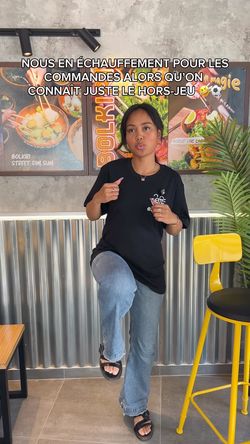 Jeune femme en tenue décontractée dans restaurant asiatique BOLKIRI avec décoration murale colorée et tabourets hauts jaunes.