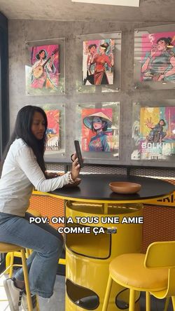 Intérieur du restaurant asiatique BOLKIRI avec femme assise à une table jaune ronde et affiches murales colorées.