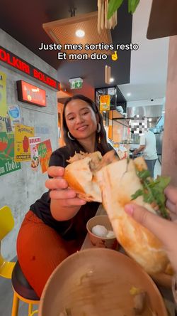 Restaurant asiatique BOLKIRI Mantes-La-Jolie avec une cliente dégustant un sandwich vietnamien dans un décor coloré.