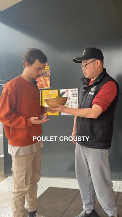 Deux personnes échangent un bol de nourriture dans un restaurant asiatique, avec un mur sombre en arrière-plan.