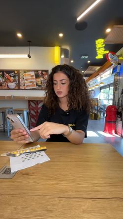 Serveuse dans un restaurant asiatique assise à une table, utilisant un smartphone, avec le menu en arrière-plan.