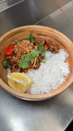 Plat asiatique dans un bol en bambou avec riz blanc, légumes, viande, coriandre et un quartier de citron.