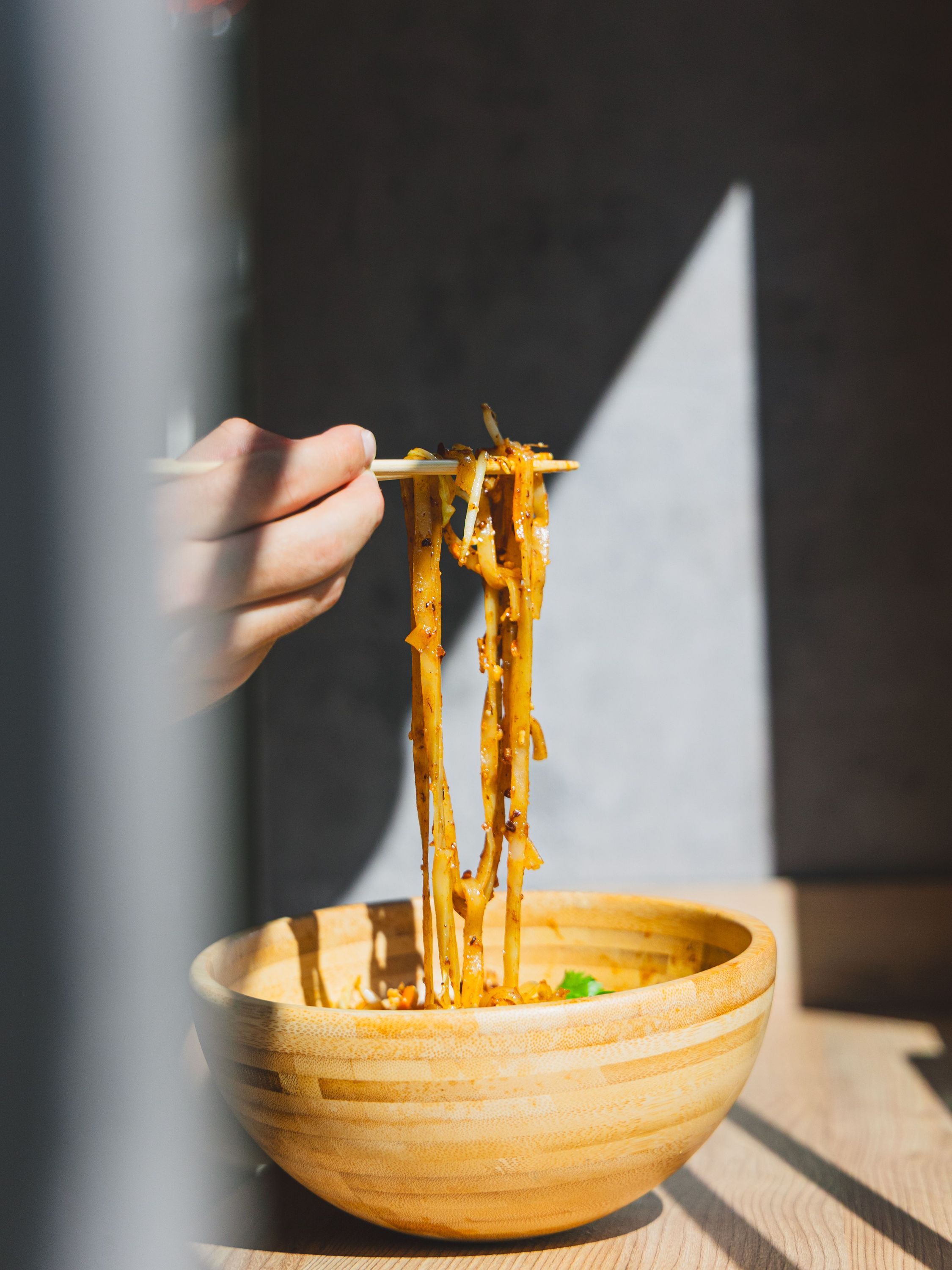 Nouilles asiatiques servies dans un bol en bois, tenues avec des baguettes dans un restaurant asiatique.
