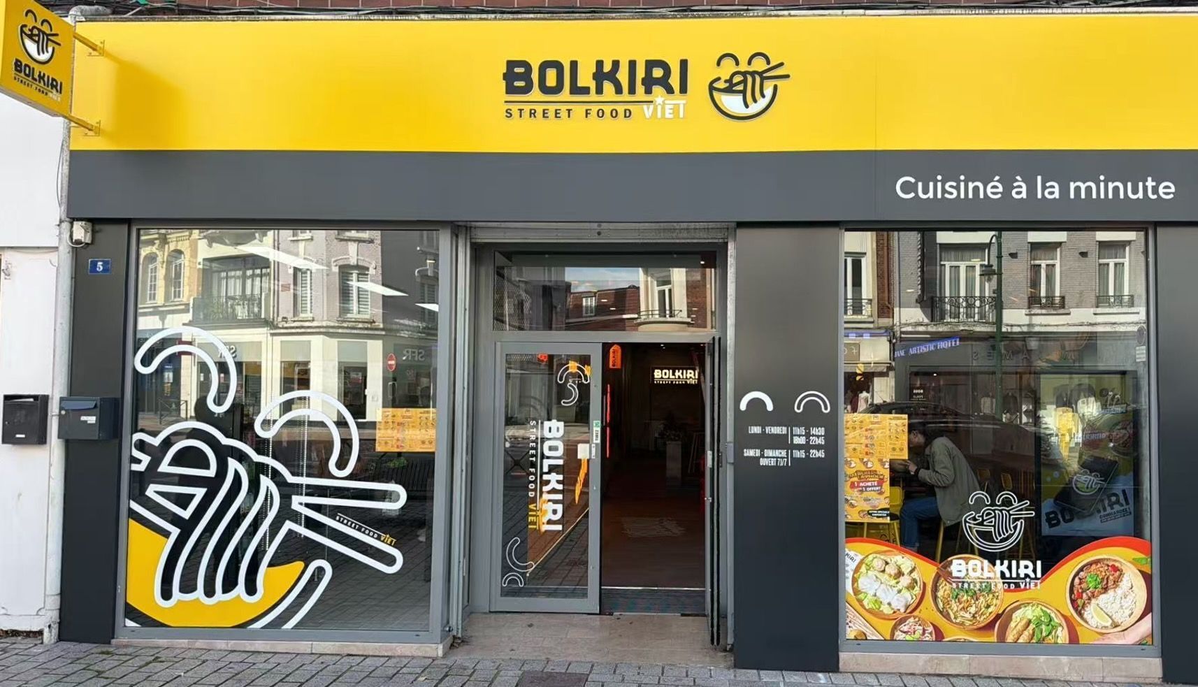 Façade moderne du restaurant asiatique BOLKIRI avec un grand logo jaune et une vitrine décorée d'illustrations de nouilles