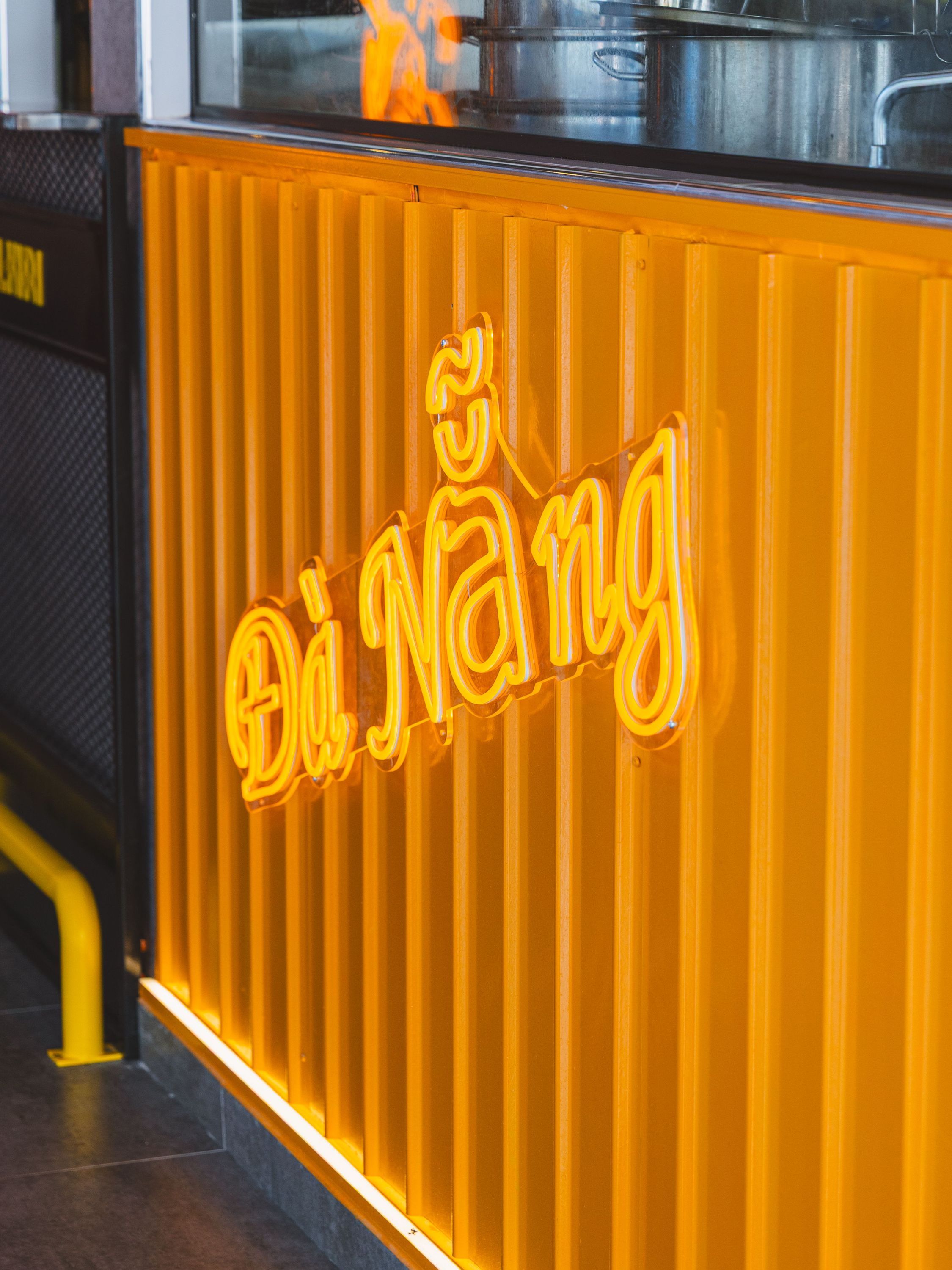 Enseigne lumineuse jaune sur un mur cannelé orange dans un restaurant asiatique.
