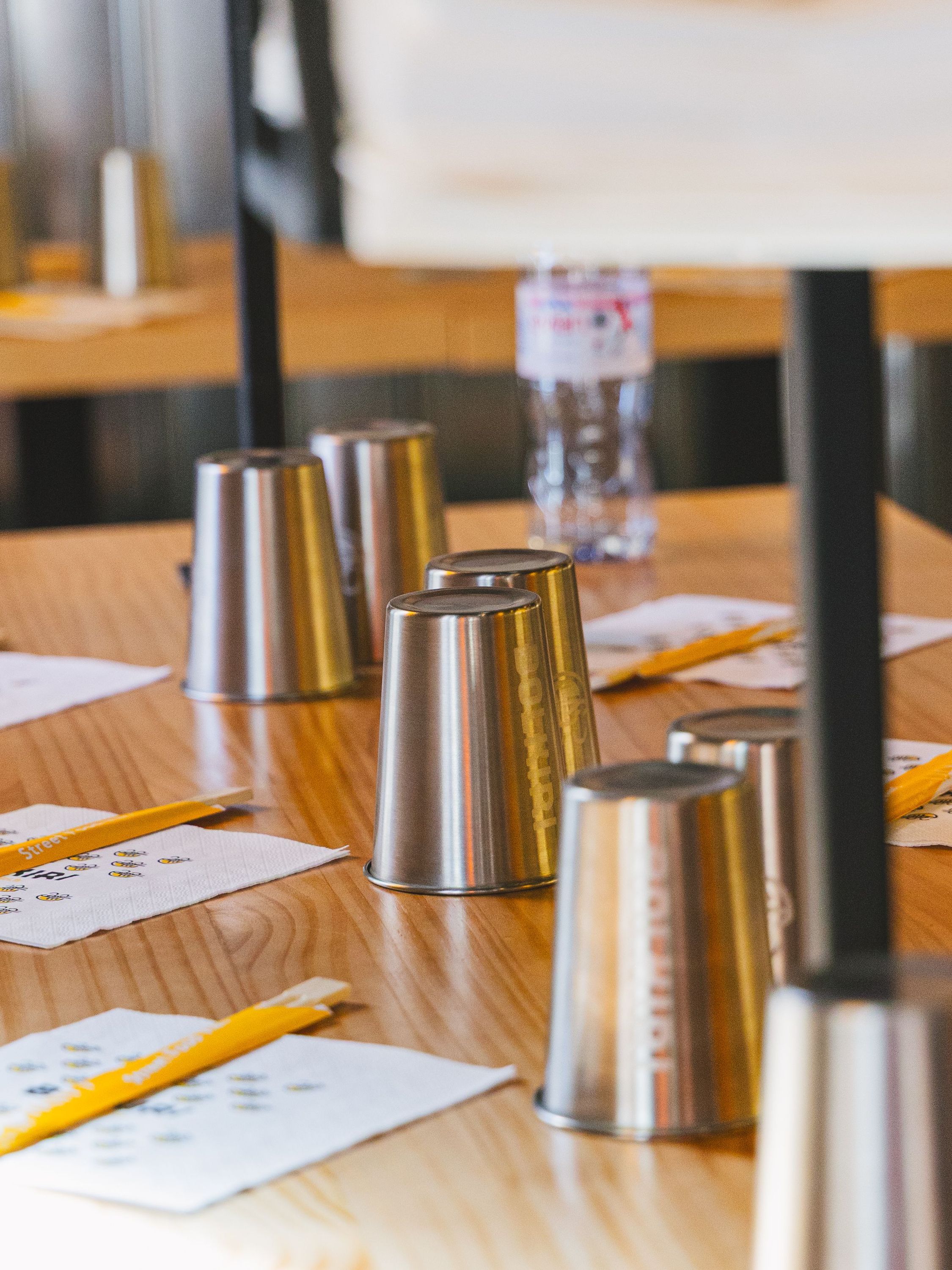 Verres en métal retournés sur une table en bois avec des baguettes et serviettes dans un restaurant asiatique.