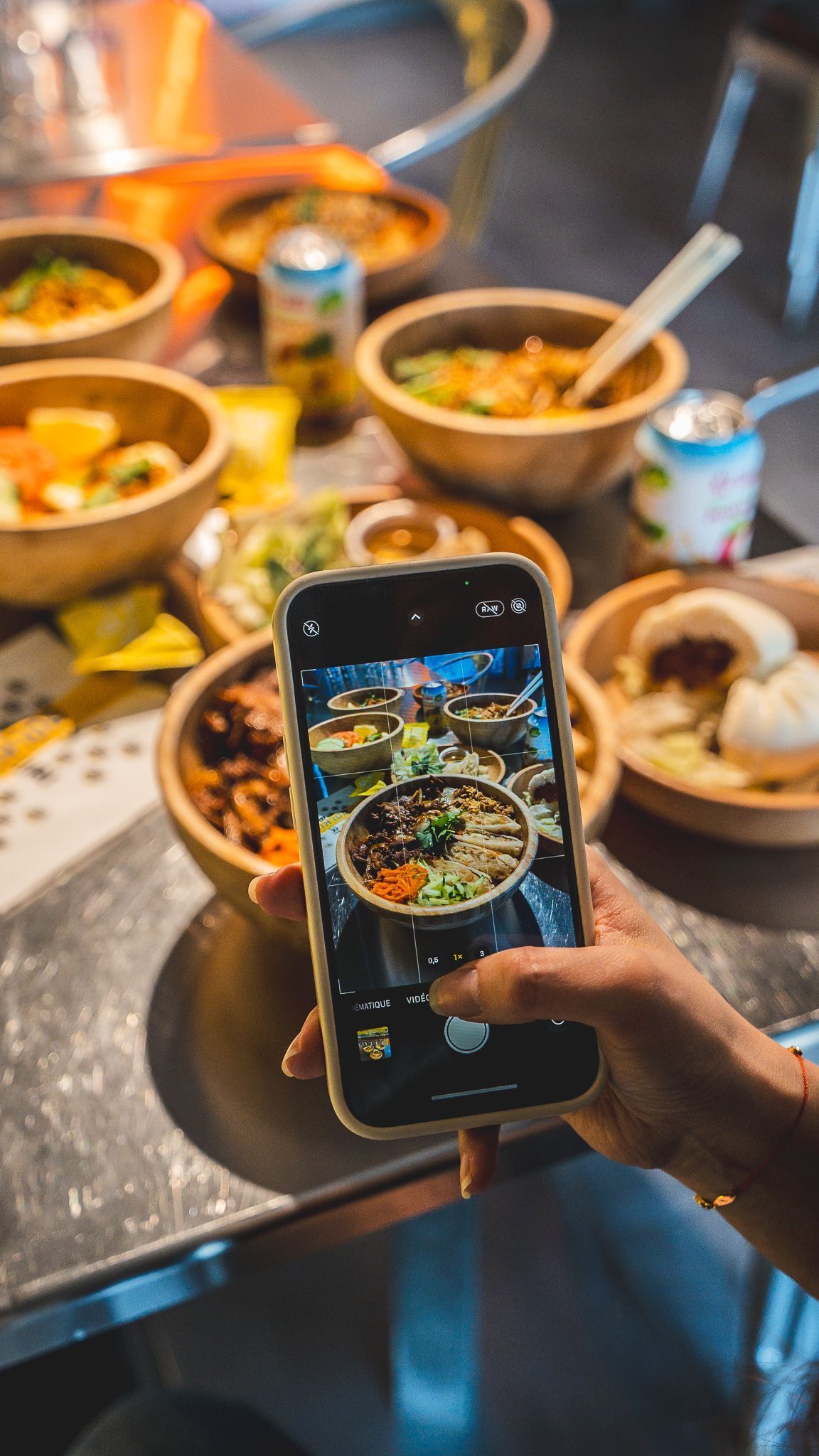 Plat asiatique dans un restaurant avec plusieurs bols, bao et cannette sur une table en métal