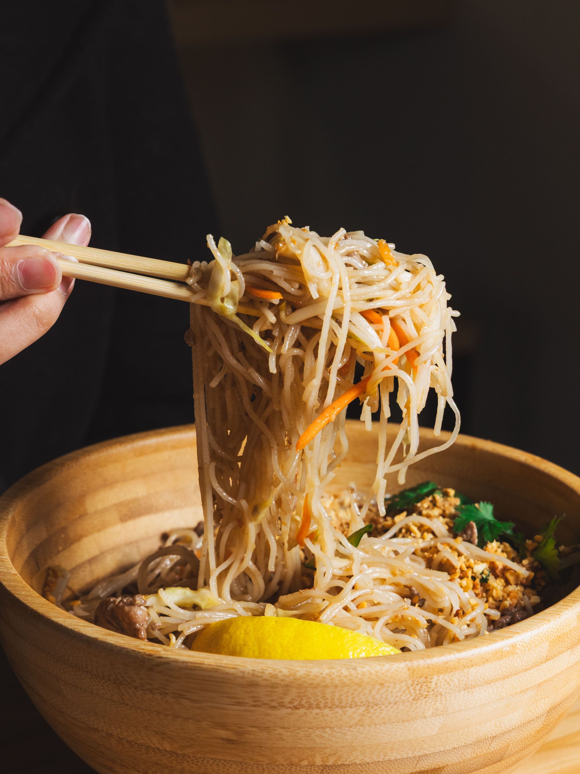 Nouilles sautées avec légumes et citron dans un bol en bois, typique d'un restaurant asiatique.