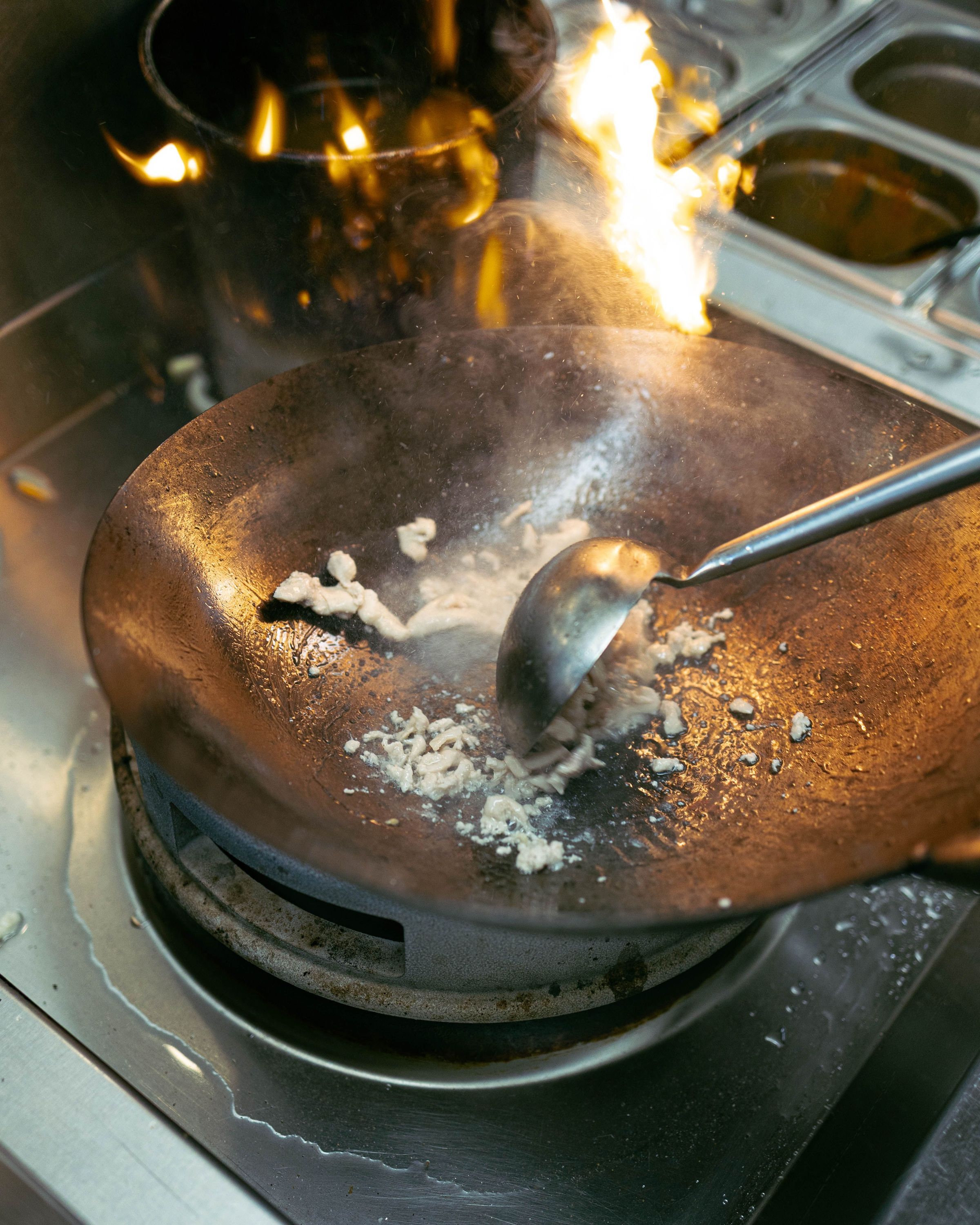 Cuisson à la poêle wok avec flamme vive dans un restaurant asiatique, morceaux de viande en train de cuire