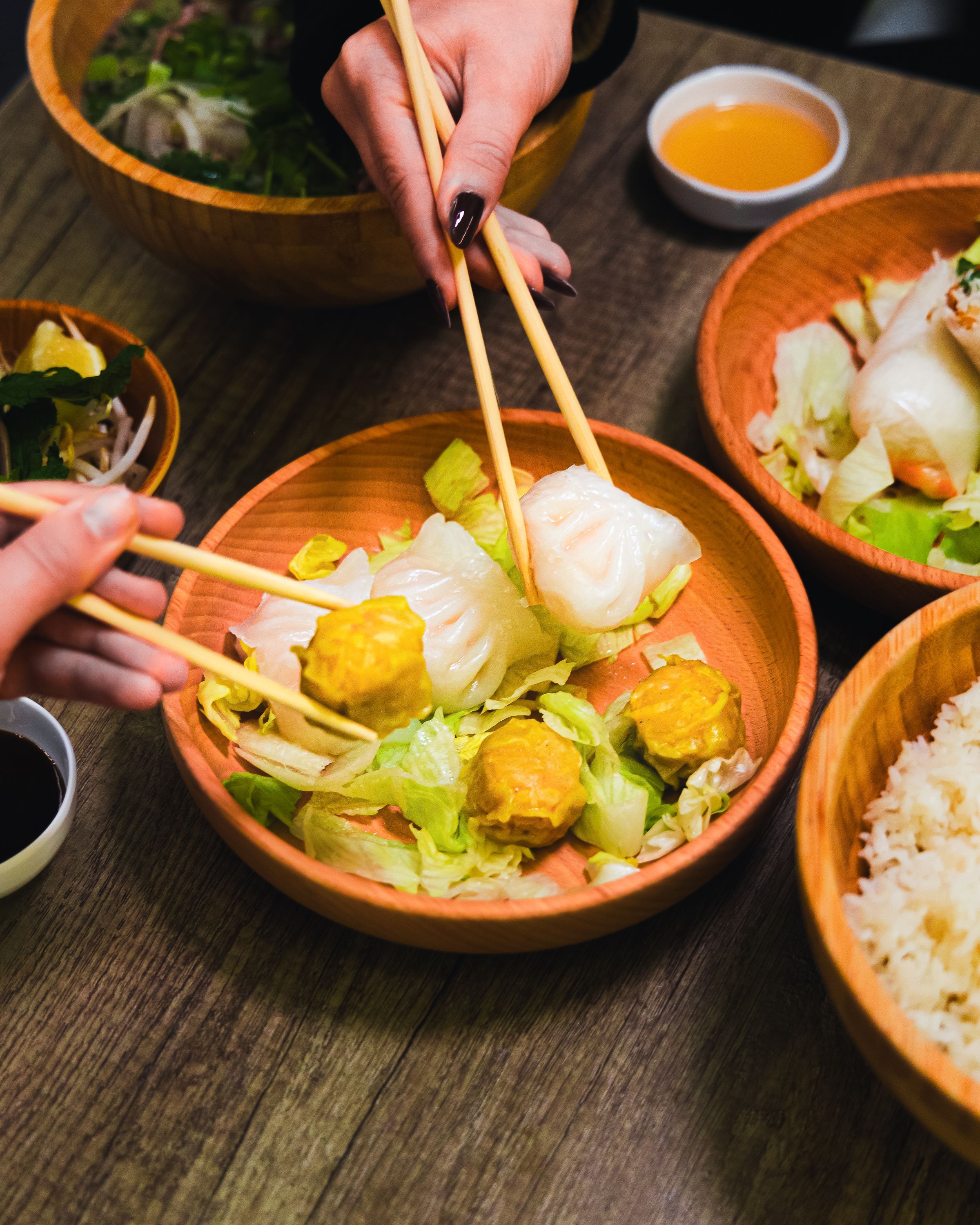 Dumplings et bouchées vapeur sur lit de laitue, accompagnés de sauces. Plat de street food asiatique.