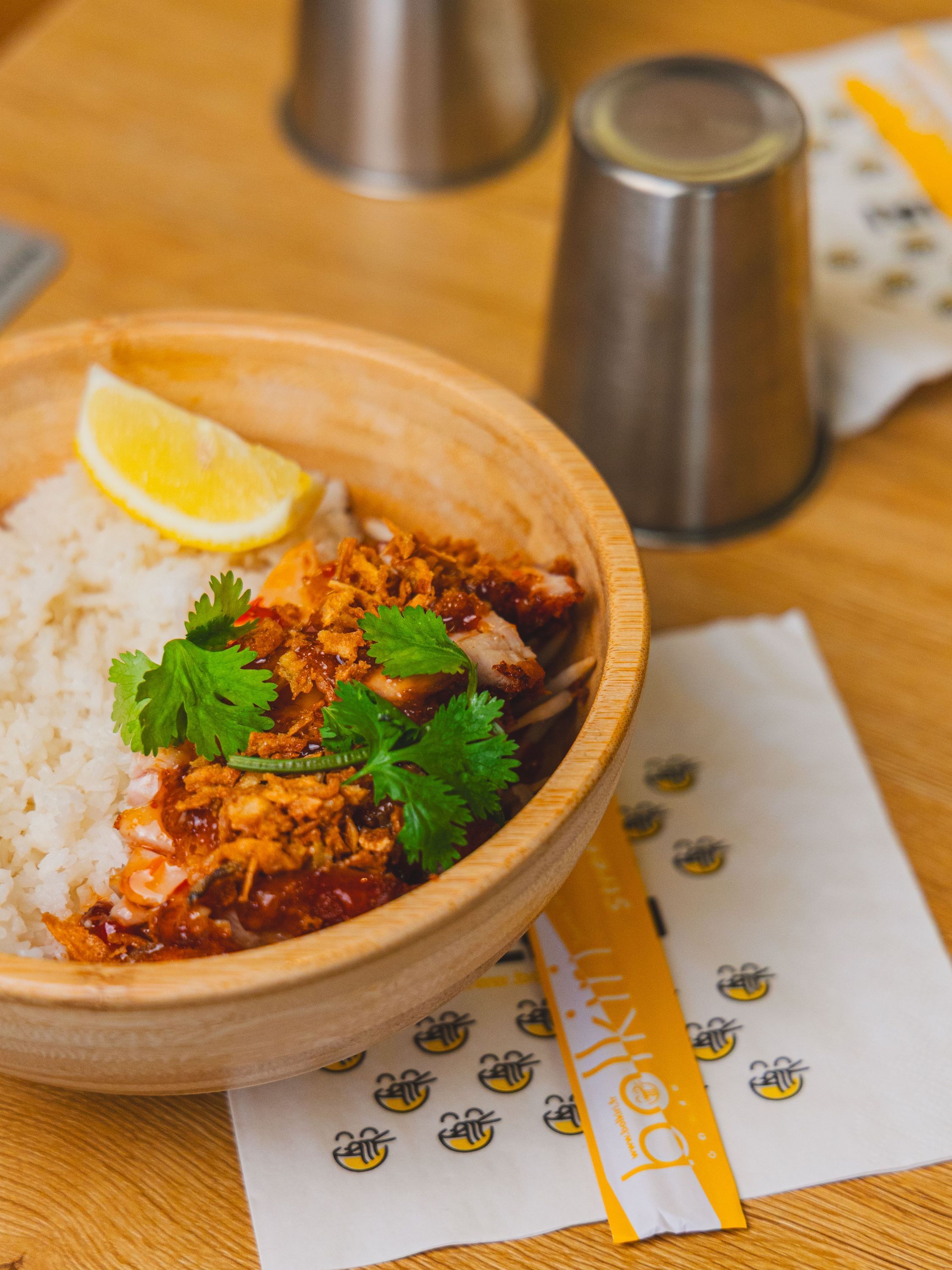 Bol de riz accompagné de viande épicée, coriandre fraîche et quartier de citron dans un restaurant asiatique.