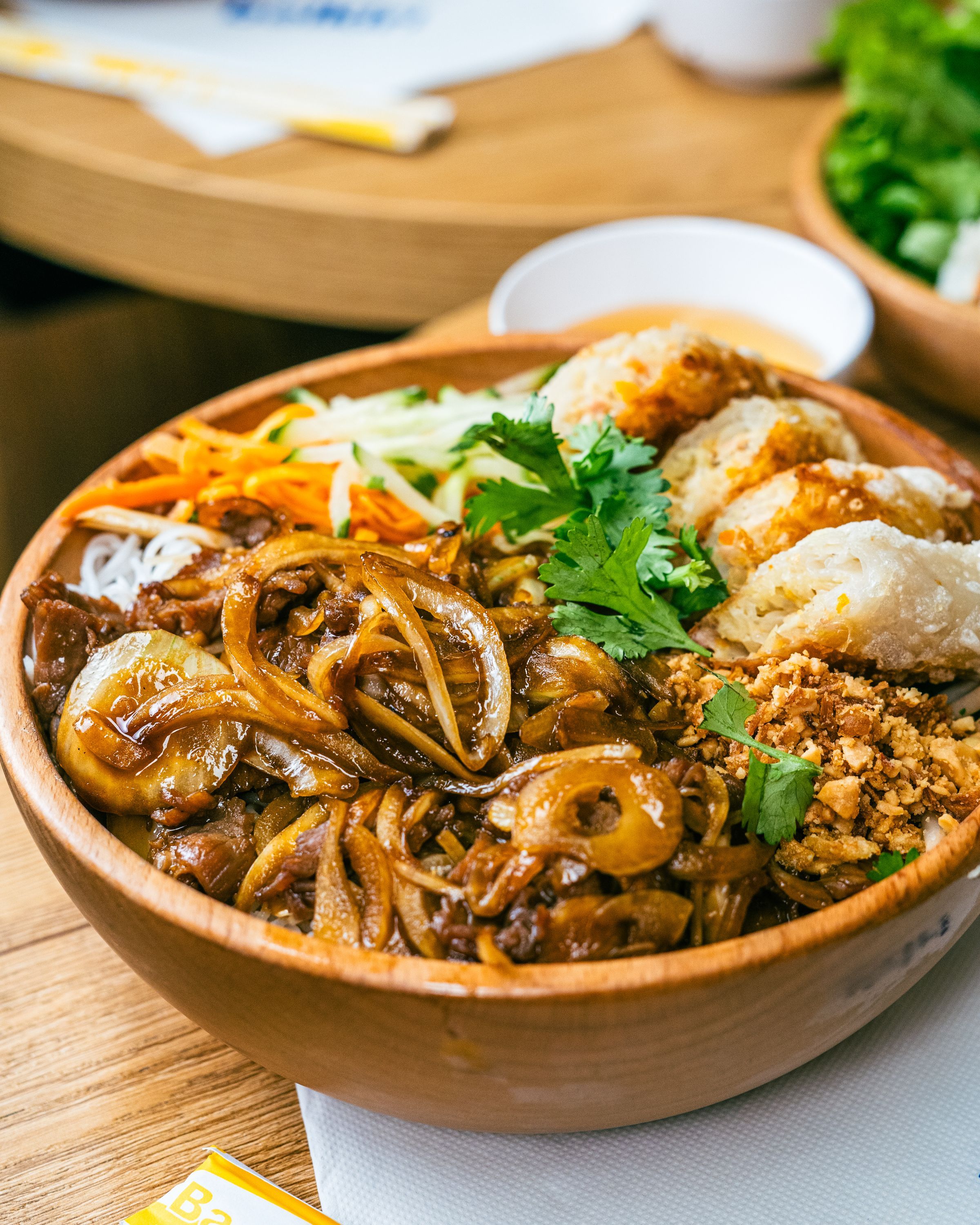 Bol de nouilles vietnamiennes avec légumes, viande, herbes fraîches et nems, typique de la street food asiatique.
