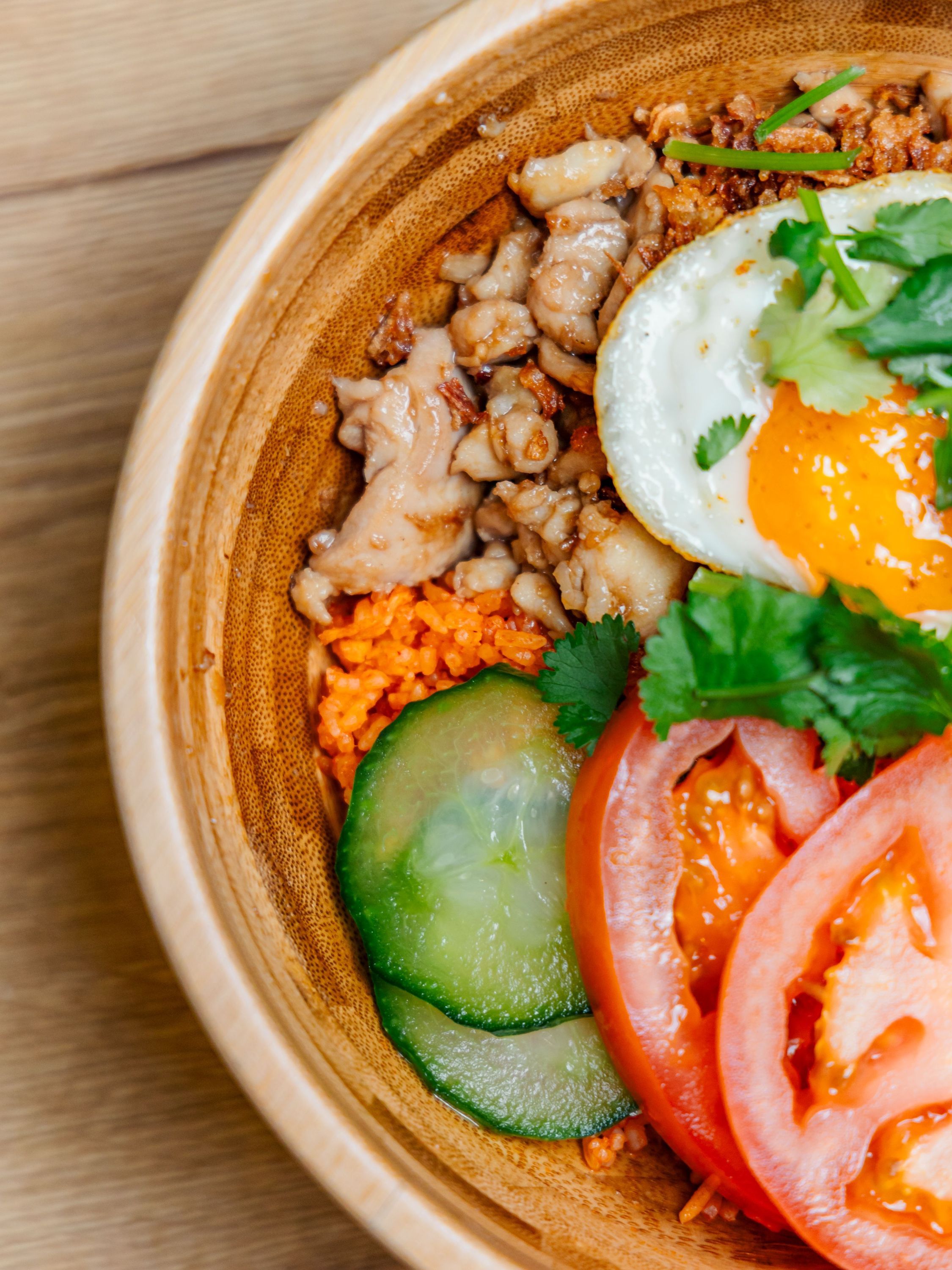 Plat asiatique avec viande hachée, œuf au plat, tranches de concombre et de tomate dans un bol en bois