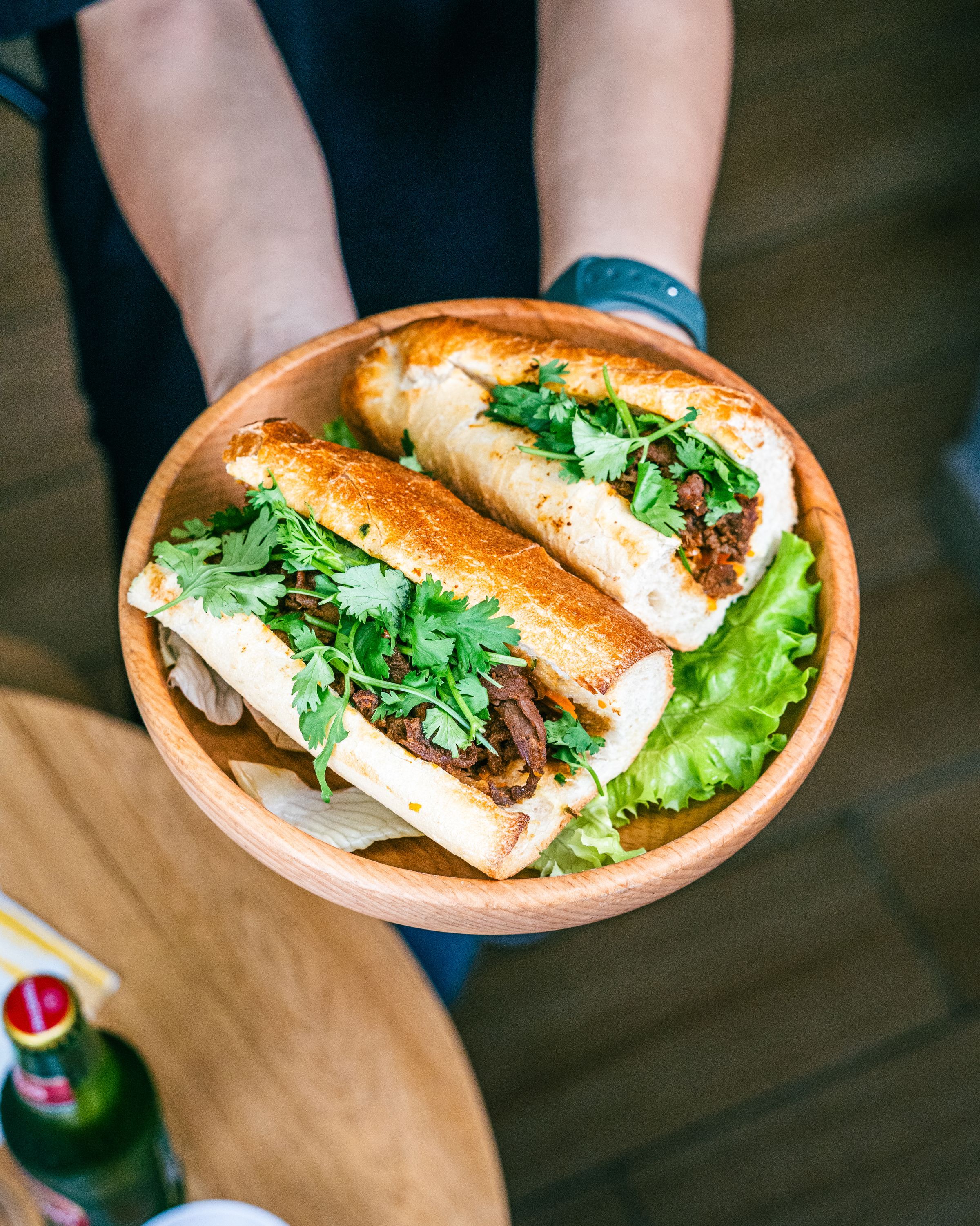 Deux baguettes vietnamiennes garnies de viande, herbes et salade, servies dans un bol en bois.