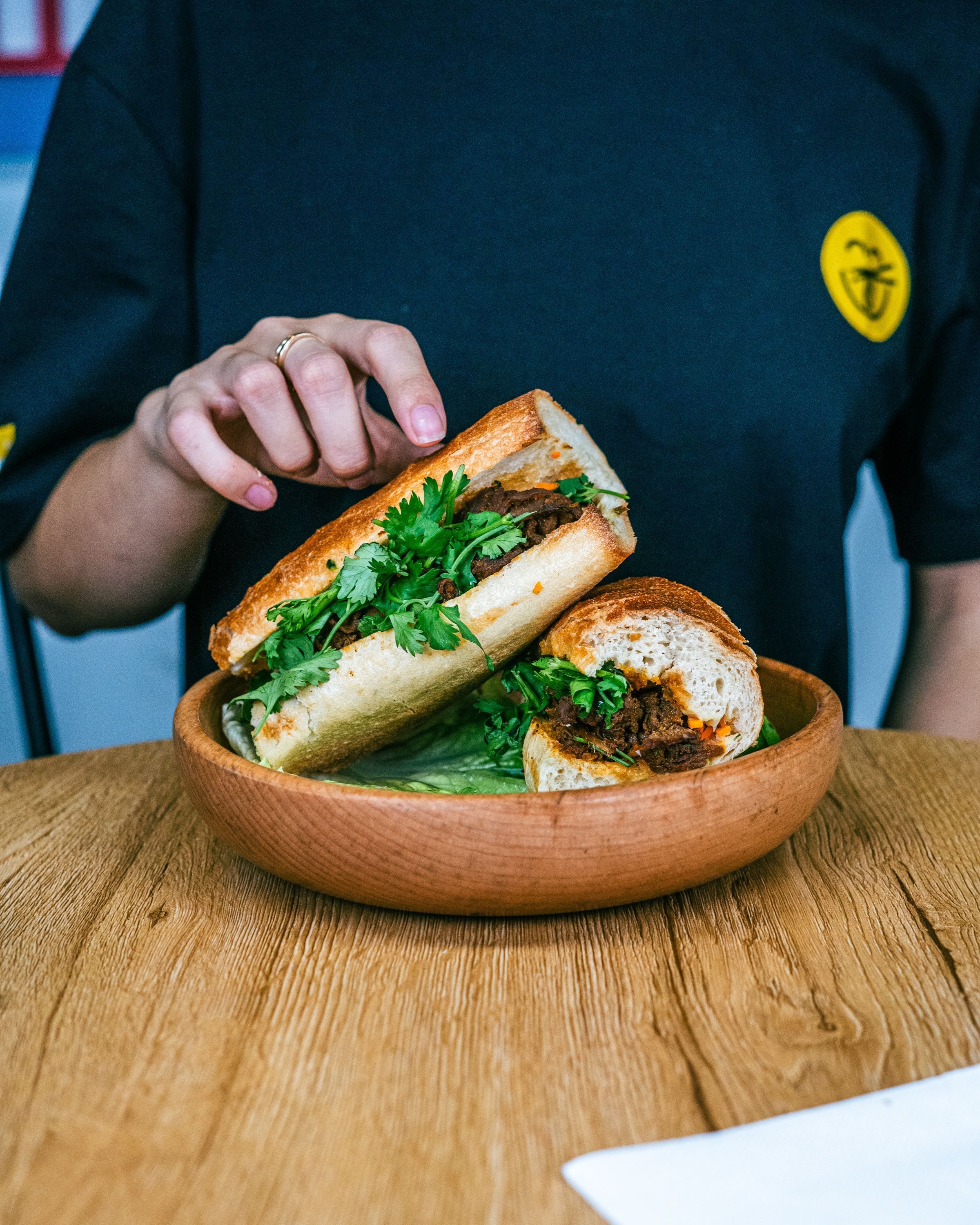 Sandwich vietnamien garni de viande et herbes, servi dans un bol en bois.