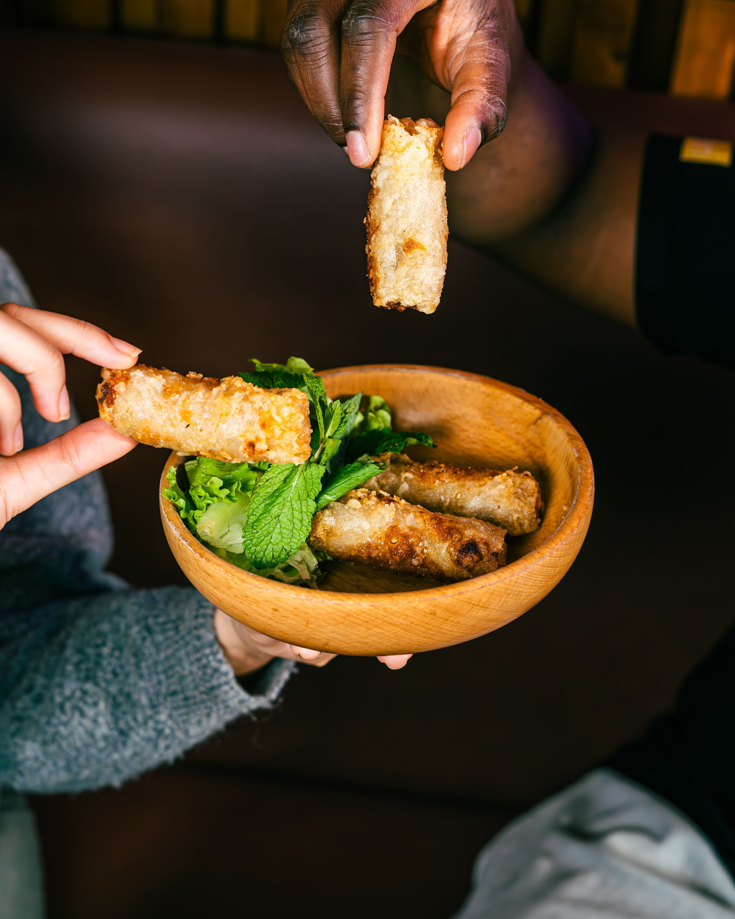 Rouleaux de printemps croustillants avec de la salade et des herbes fraîches dans un bol en bois.