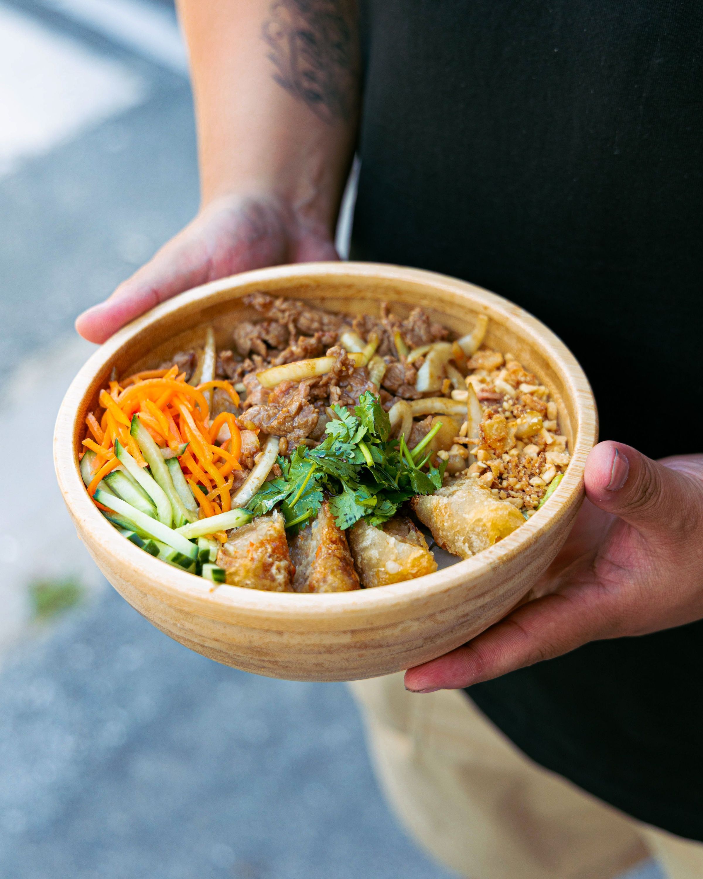 Plat asiatique dans un bol en bois avec viande, légumes frais, rouleaux de printemps et herbes.