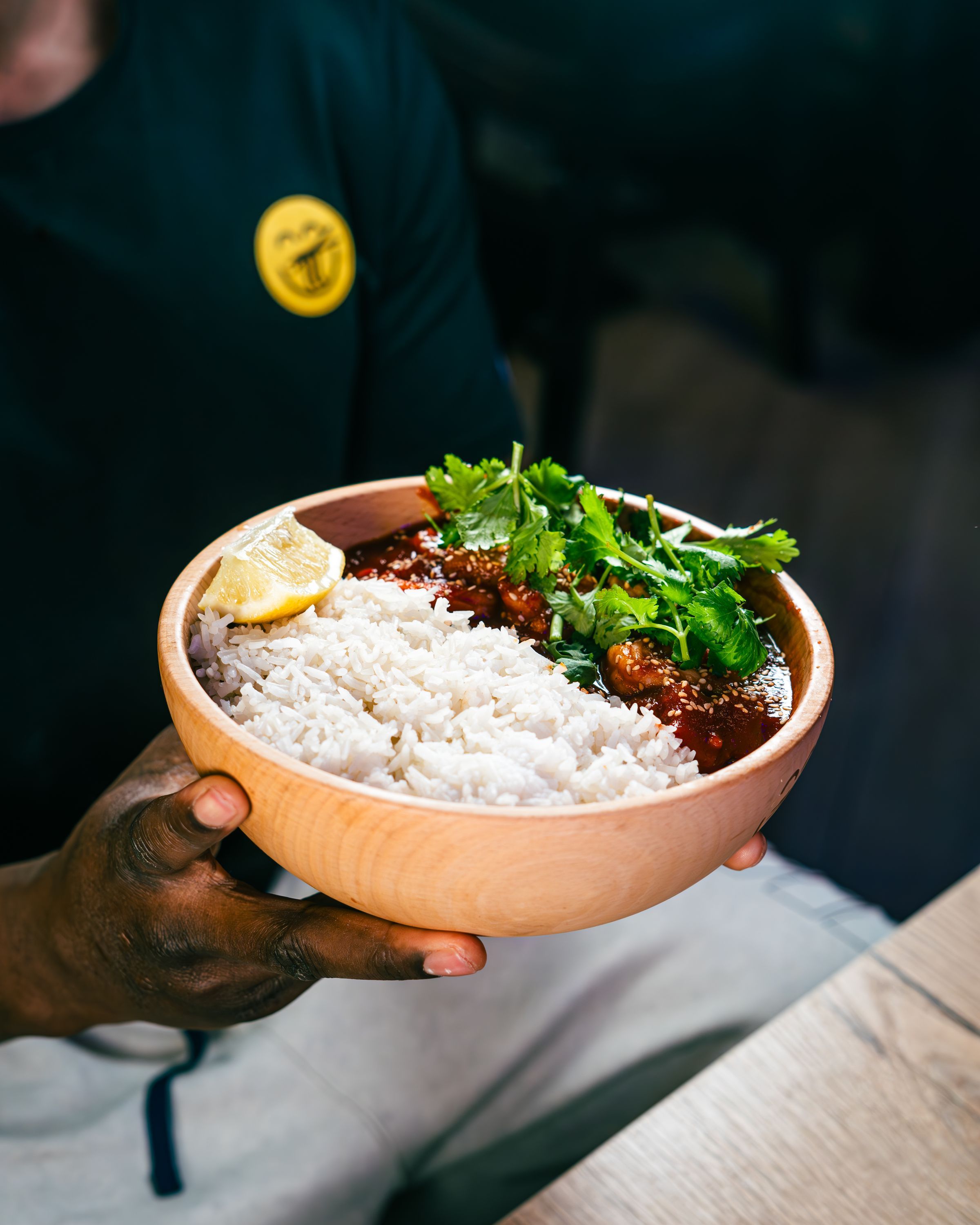 Bol en bois contenant du riz, des boulettes de viande, sauce épicée et coriandre, servi avec un quartier de citron.