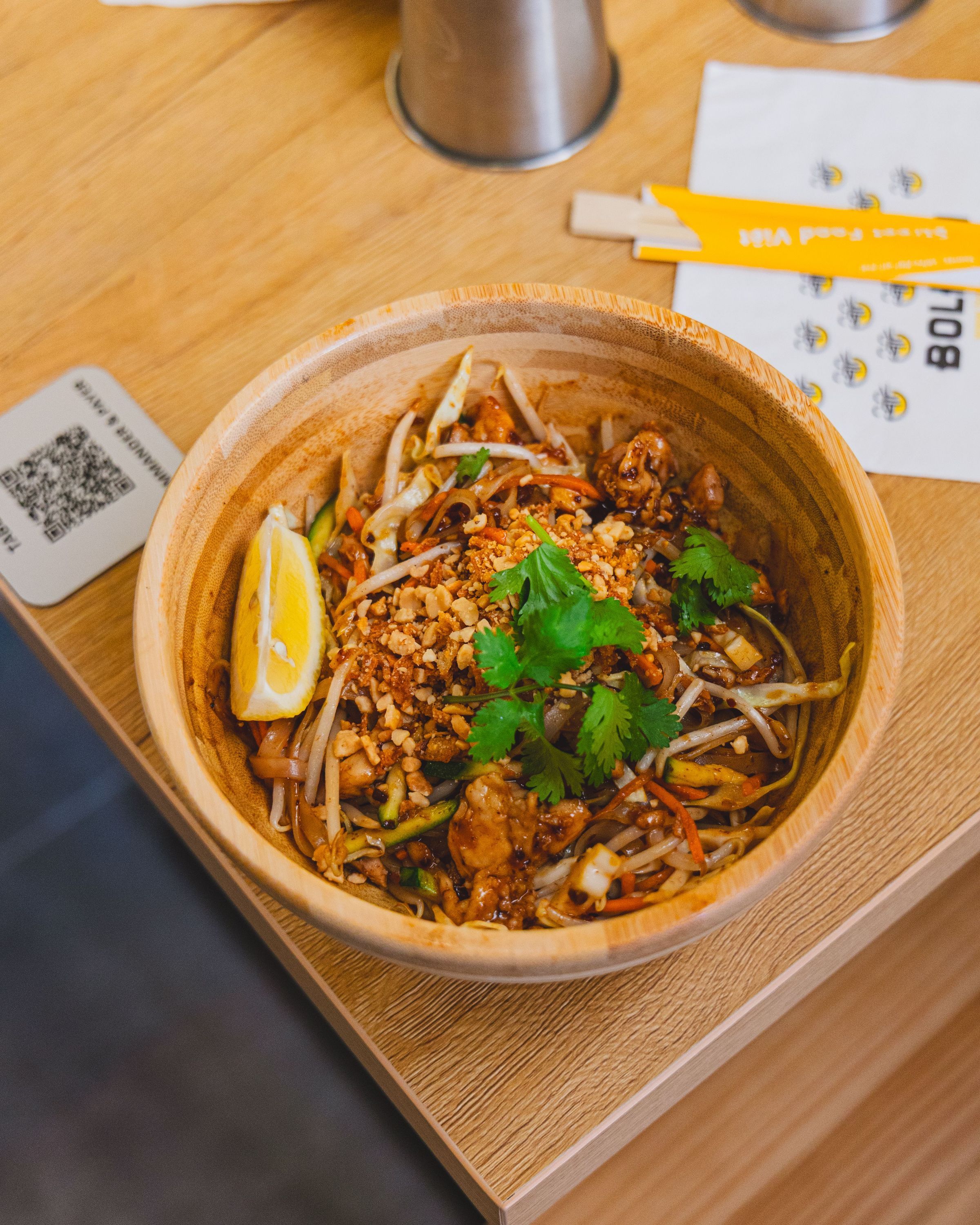 Plat asiatique servi dans un bol en bois avec des légumes, noix et herbes fraîches sur une table en bois claire