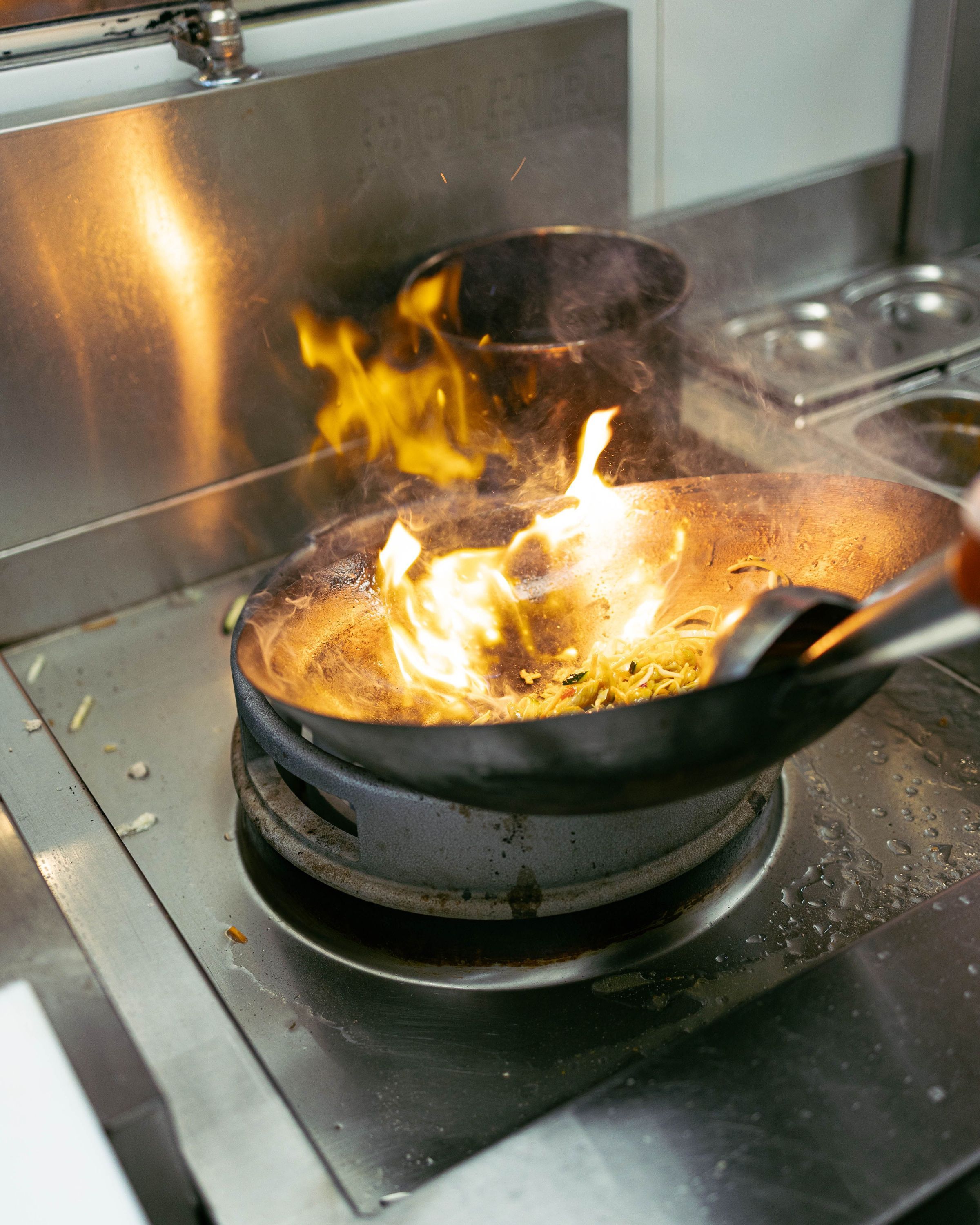 Wok en acier inoxydable avec flammes vives sur une cuisinière dans un restaurant asiatique
