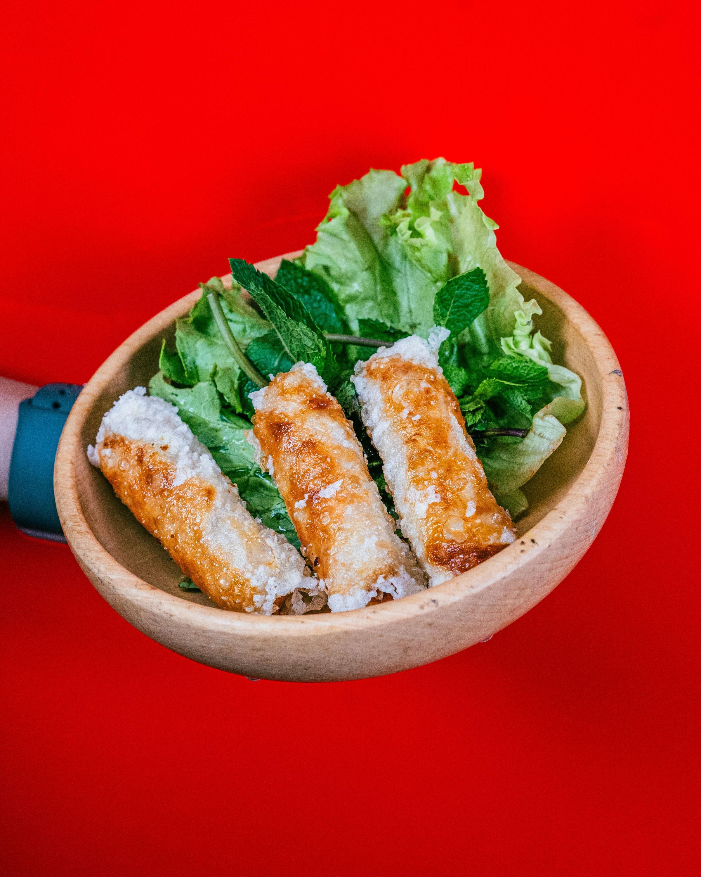 Nem frit servi dans un bol en bois avec laitue et feuilles de menthe, plat typique d'un restaurant asiatique