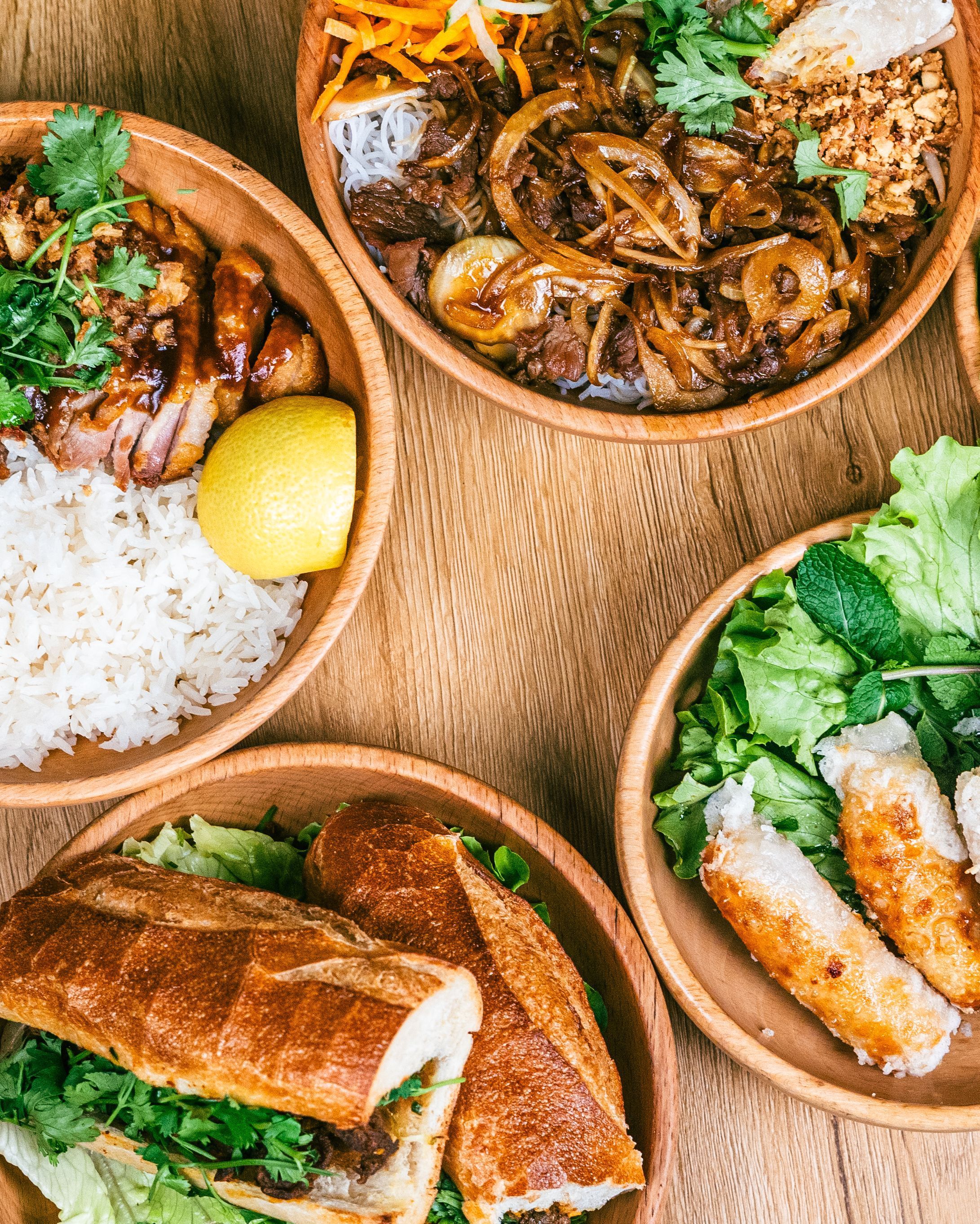 Assortiment de plats asiatiques, incluant du riz, des rouleaux, et un sandwich dans des bols en bois.