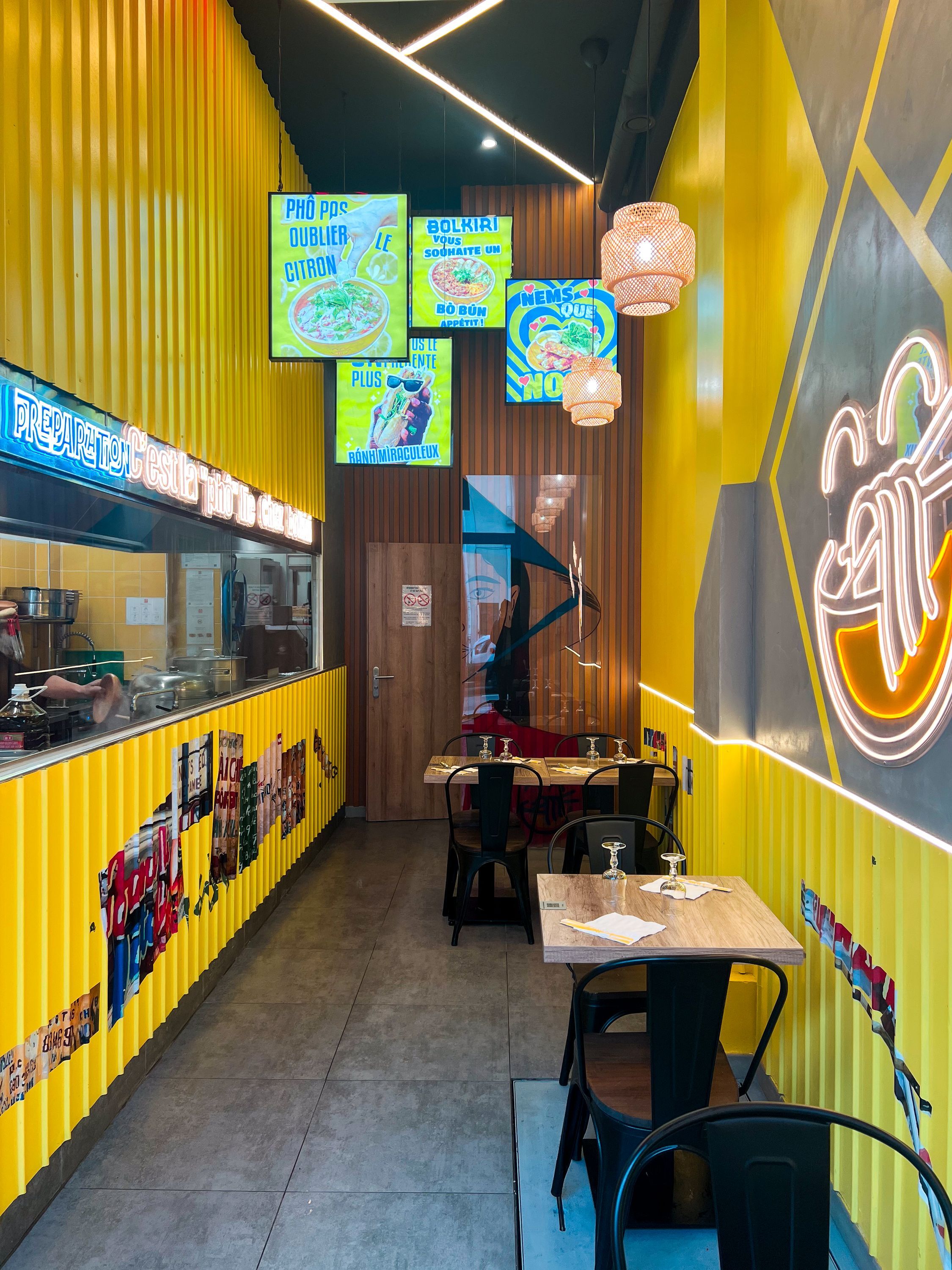 Ambiance lumineuse avec des murs jaunes, sièges en métal et affiches de street food vietnamienne.