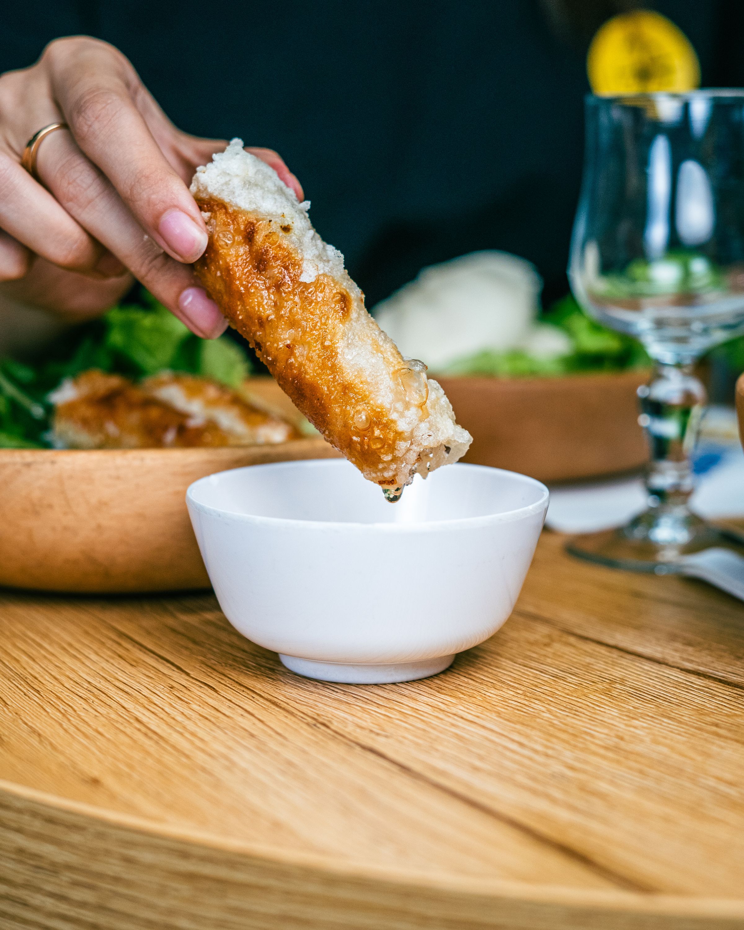 Rouleau de printemps croquant trempé dans une petite sauce blanche, accompagné de salade.
